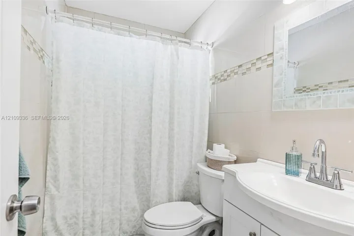 Bathroom featuring full-height wall tiling with mosaic accent banding, white vanity cabinet with an integrated sink, polished chrome faucet, and a wall-mounted mirror with a tiled frame