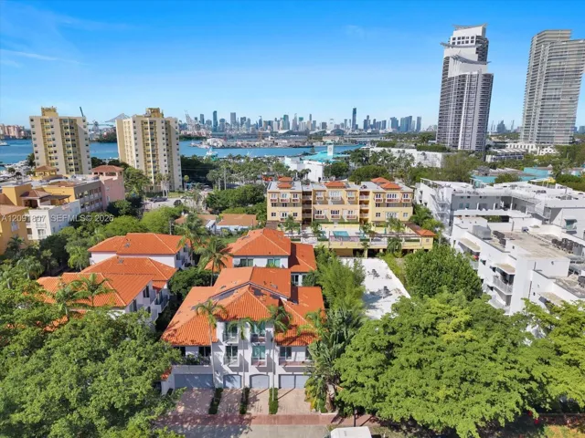 Aerial perspective of a multi-story residential building featuring a red-tile roof, white exterior cladding, integrated garage doors, and mature landscaping