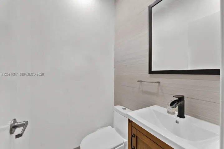 Vanity with a wooden cabinet base and integrated rectangular basin, matte black faucet, framed mirror, and textured tile wall accents