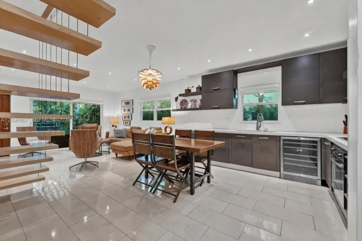Open-concept kitchen and living area featuring a floating staircase with wood treads, high-gloss cabinetry, built-in wine refrigeration, large-format tile flooring, and recessed ceiling lighting