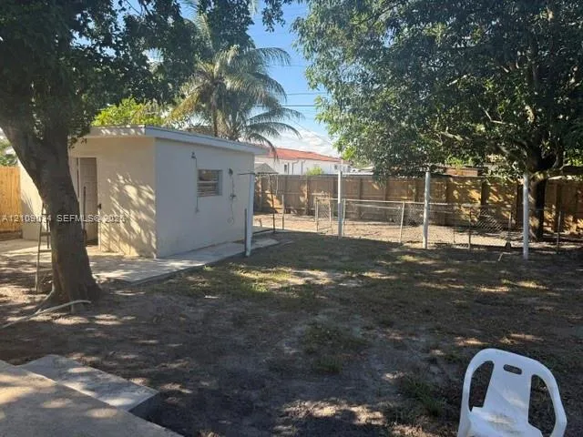 Backyard featuring a standalone stucco structure, concrete patio, perimeter wood fencing, and mature trees