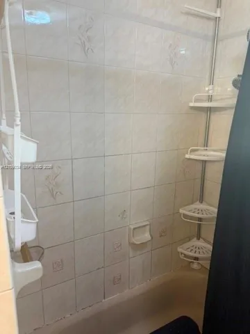 Shower area featuring neutral tile wall surround, integrated soap dish, and a tub basin