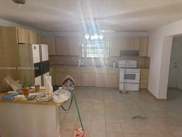 Kitchen featuring light-finish wood cabinetry, a peninsula, tile flooring, and integrated white appliances including a range and double-door refrigerator