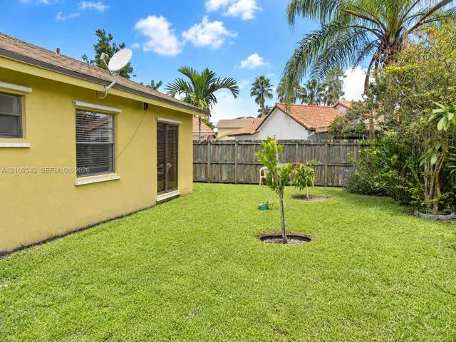 Fenced backyard featuring a manicured lawn, established landscaping, and sliding glass door access
