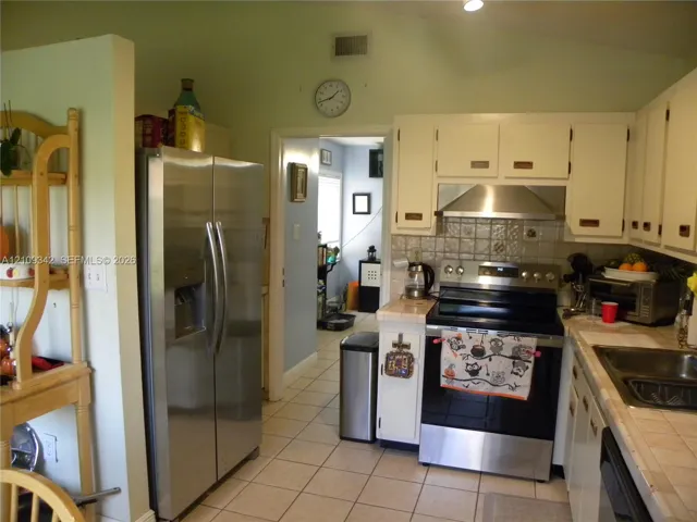 Kitchen featuring white cabinetry, tile countertops, stainless steel side-by-side refrigerator, stainless steel range with integrated hood, and tile flooring