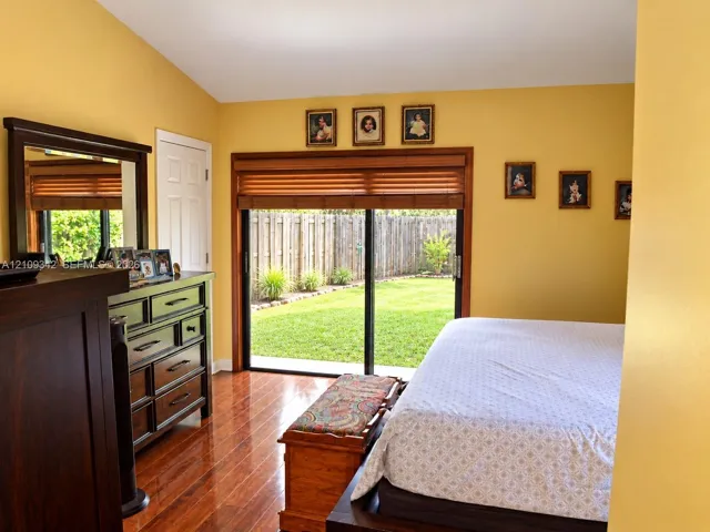 Room featuring wood-finish flooring, vaulted ceilings, and sliding glass doors with wood-slat blinds opening to a fenced backyard