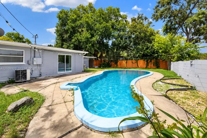 Backyard featuring a free-form swimming pool, concrete patio, wood privacy fencing, and masonry perimeter wall