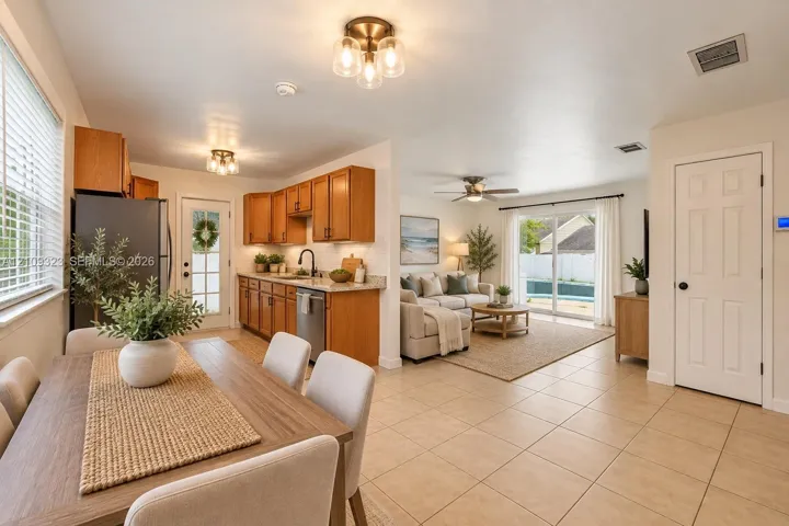 Kitchen featuring medium-toned wood cabinetry, stone countertops, stainless steel appliances, neutral tile flooring, and sliding glass doors