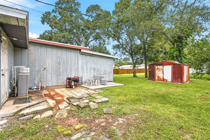 Expansive rear yard featuring mature trees, a detached metal storage structure, and a concrete patio area