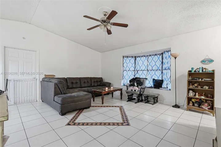 Living area featuring vaulted ceilings, white tile flooring with decorative inlay, a bay window, and a ceiling fan