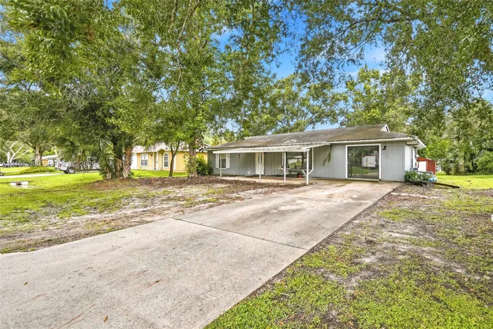 Single-story exterior featuring gray siding, a covered front porch, and a concrete driveway shaded by mature trees