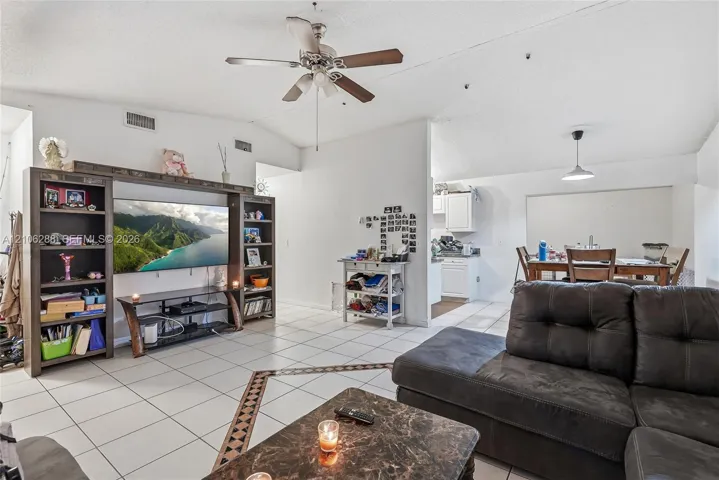 Open-concept interior featuring vaulted ceilings, oversized white floor tile with decorative border inlay, and a built-in media center with integrated shelving