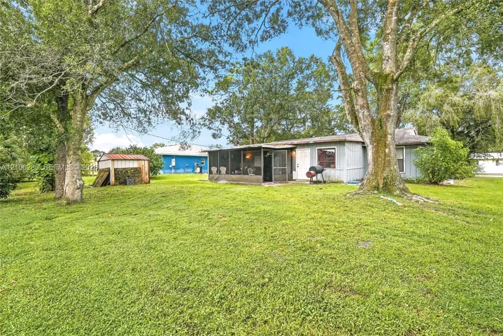 Expansive grounds featuring mature shade trees, a detached storage structure with a metal roof, and a screened-in porch