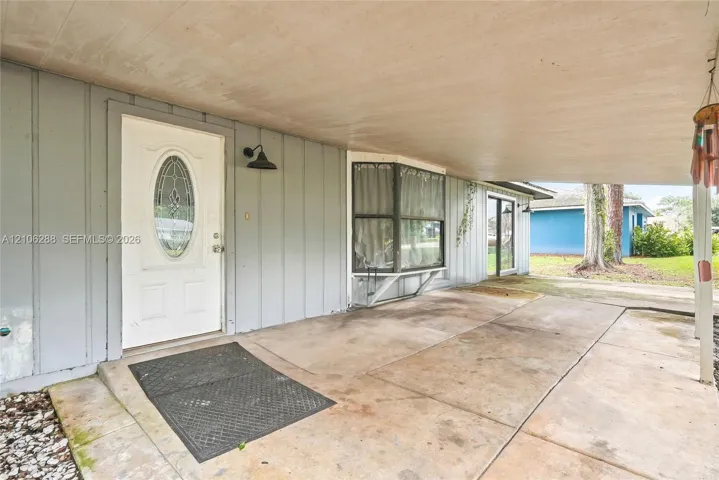 Covered concrete entryway featuring vertical siding, a door with an oval decorative glass insert, a bay window, and exterior wall-mounted gooseneck lighting