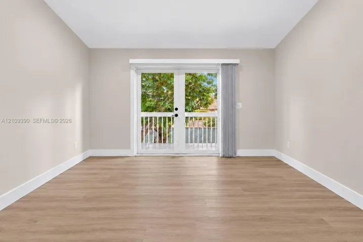 Neutral interior room featuring wood-finish flooring, white walls, and French doors opening to an exterior balcony