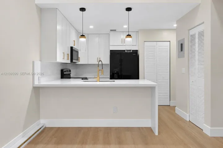 Kitchen featuring white shaker-style cabinetry, quartz countertops, a gold-toned pull-down faucet, dual glass pendant lights, and wood-finish flooring