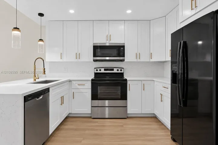 Kitchen featuring white Shaker-style cabinetry, quartz countertops, wood-finish flooring, gold-tone hardware, and two cylindrical glass pendant lights