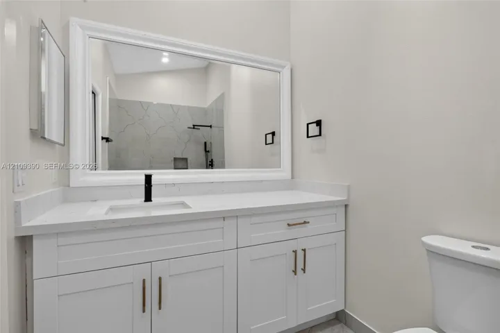 White cabinetry with brass-toned hardware, quartz countertop, undermount sink with matte black faucet, and framed vanity mirror