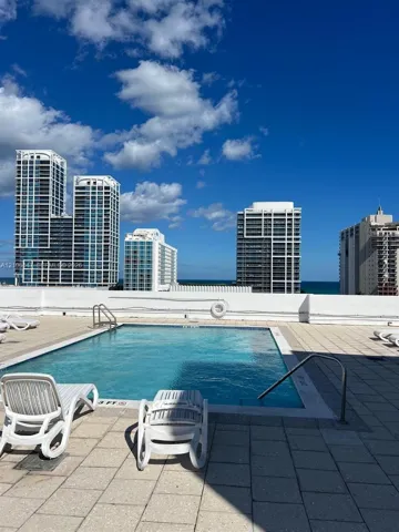 Rooftop pool with tile surround, metal handrails, and surrounding urban skyline