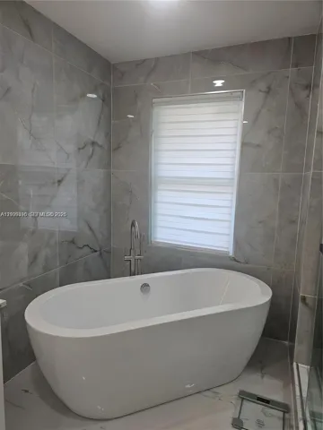 Freestanding soaking tub featuring a chrome floor-mounted faucet and large-format porcelain wall tile with a neutral-toned veined pattern