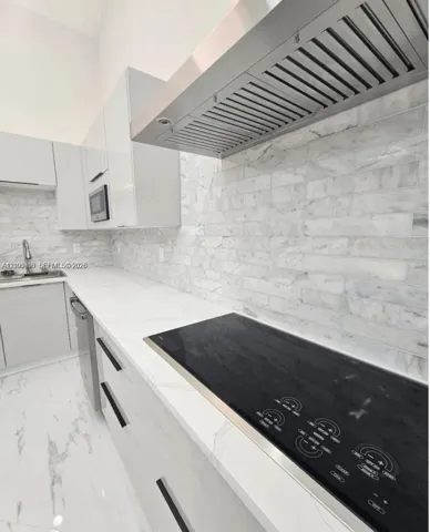 Contemporary kitchen featuring high-gloss cabinetry, stone-finish countertops, subway tile backsplash, a stainless steel range hood, and integrated electric cooktop