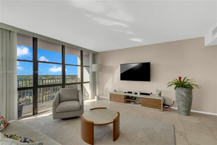 Living area featuring floor-to-ceiling windows, natural stone tile flooring, and a private balcony with metal railing