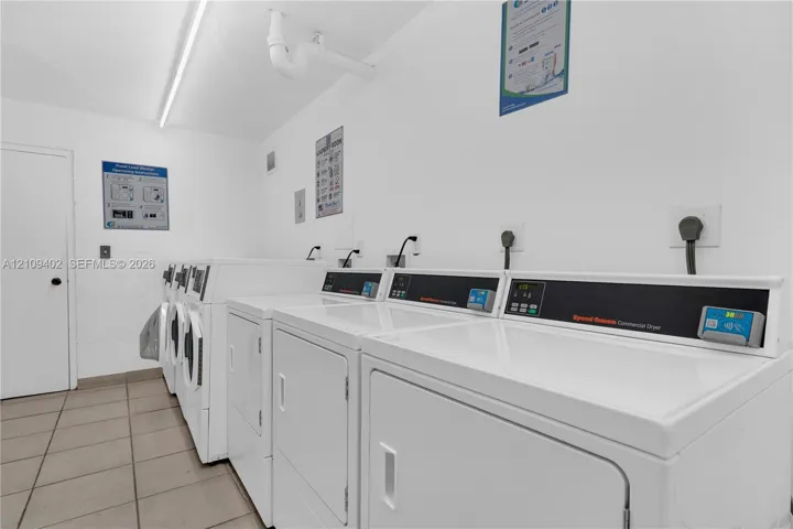 Laundry facility featuring multiple high-capacity commercial-grade dryers, tiled flooring, and industrial-style linear lighting