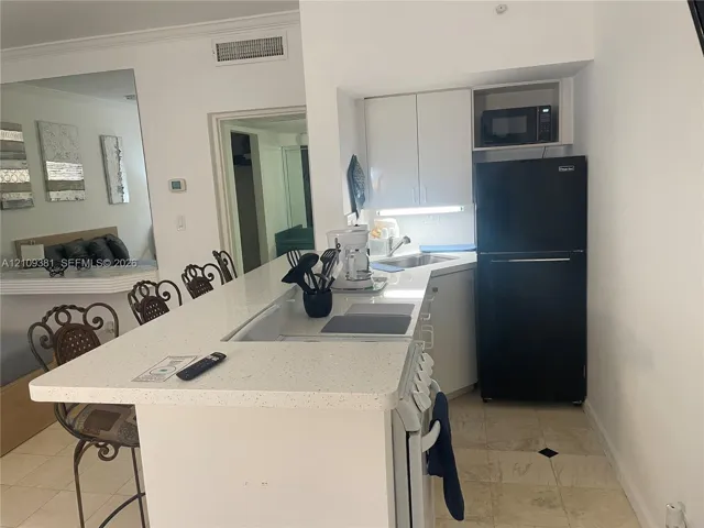 Kitchen area featuring a quartz countertop peninsula, white cabinetry, a built-in microwave, a stainless steel sink, and light-toned tile flooring
