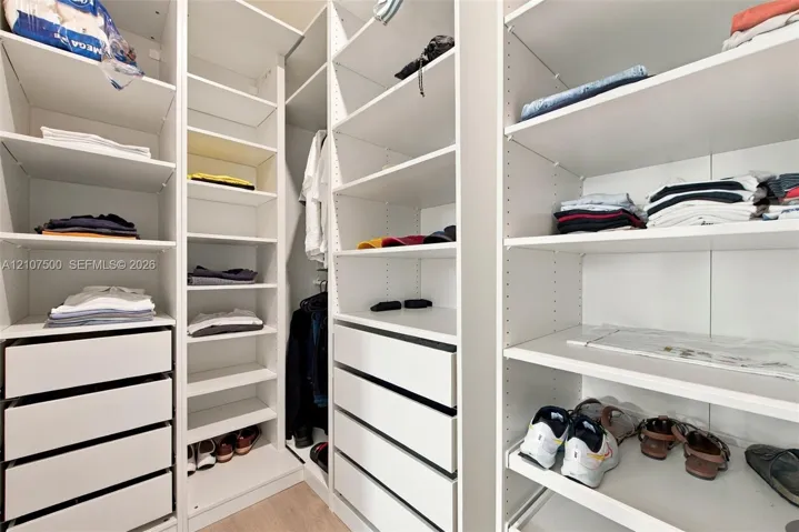 Custom closet system featuring white built-in shelving, adjustable storage racks, integrated cabinetry, and multi-tier drawer units