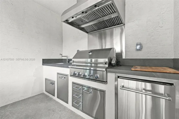 Outdoor kitchen featuring stainless steel built-in grill, professional-grade range hood, stone-finish countertops, stainless steel under-counter cabinetry, and integrated prep sink with faucet