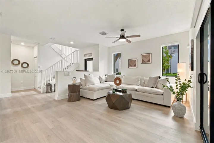 Open-concept interior featuring wood-finish flooring, a white staircase with a vertical balustrade, recessed lighting, a ceiling fan with integrated lighting, and glass sliding doors