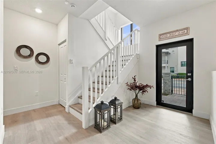 Foyer featuring wood-finish flooring, a glass-panel entry door, and a staircase with white painted balusters and wood-finish treads