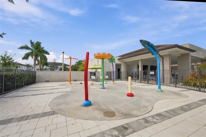 Splash pad featuring integrated water spray fixtures, concrete surfacing, paver patio, and metal perimeter fencing
