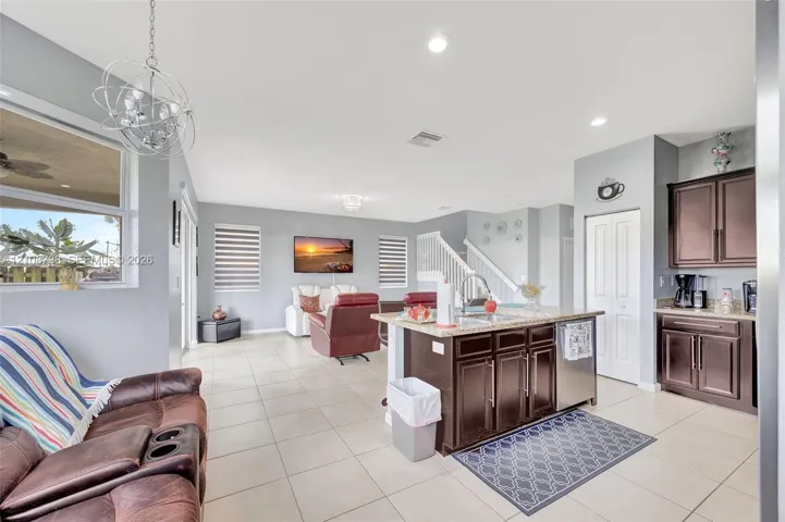 Open-concept interior featuring large-format tile flooring, a kitchen island with stone surfacing, espresso-toned cabinetry, recessed lighting, and a modern sculptural pendant fixture