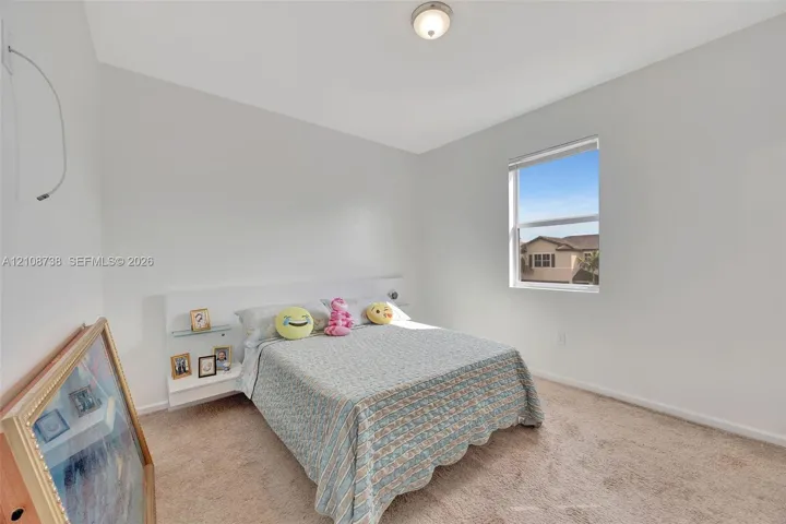 Neutral-toned walls, high ceilings, carpeted flooring, built-in headboard with integrated shelving, and a single-pane window