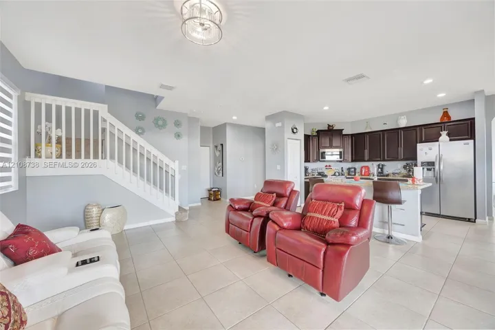 Open-concept interior featuring tile flooring, a white staircase with a vertical baluster railing, dark-toned cabinetry, stainless steel kitchen appliances, and recessed lighting