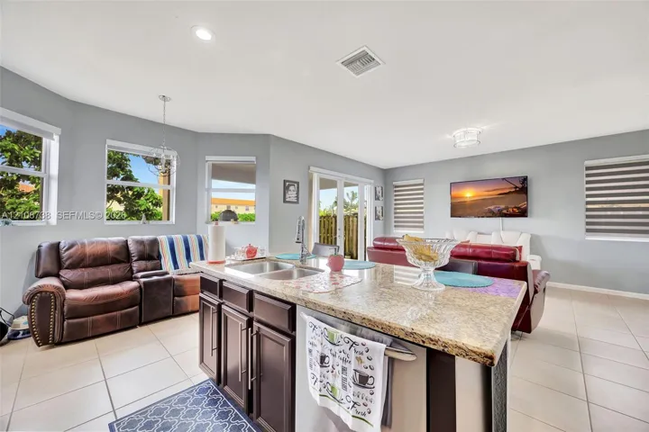 Kitchen island featuring a stone countertop, dual-basin stainless steel sink, and dark-toned cabinetry, complemented by tile flooring and recessed lighting