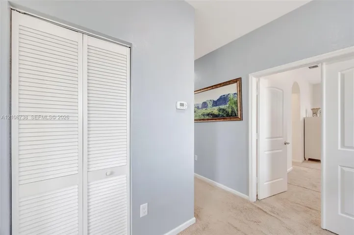 Interior hallway featuring white louvered-style bi-fold doors, neutral wall paint, and arched doorway entry