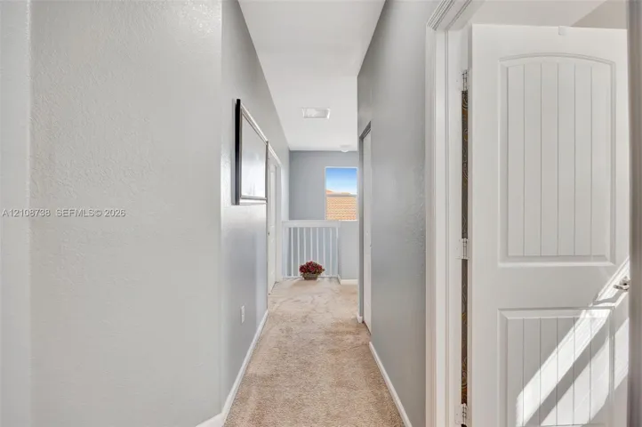 Hallway featuring neutral-toned carpeting, two-panel interior doors, light-colored wall paint, and a decorative railing