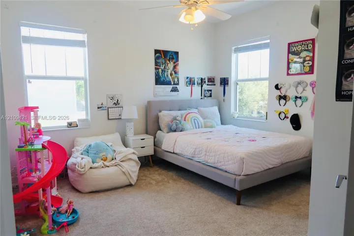 Bedroom featuring neutral carpeted flooring, dual windows with blinds, and a ceiling fan with integrated lighting