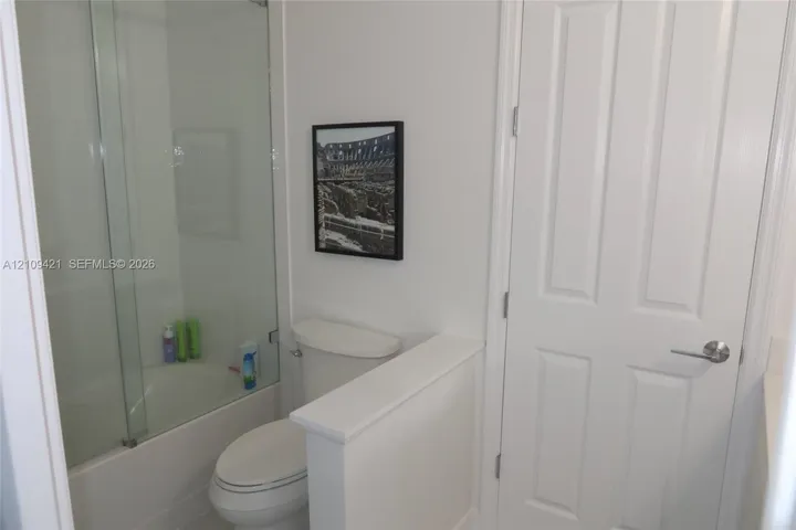 Bathroom featuring a glass shower panel, tub with tiled surround, and a white interior door with brushed metal hardware