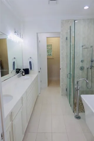 Dual-sink vanity with a solid-surface countertop, glass-enclosed walk-in shower with multi-head fixtures, freestanding soaking tub with floor-mounted faucet, and polished tile flooring