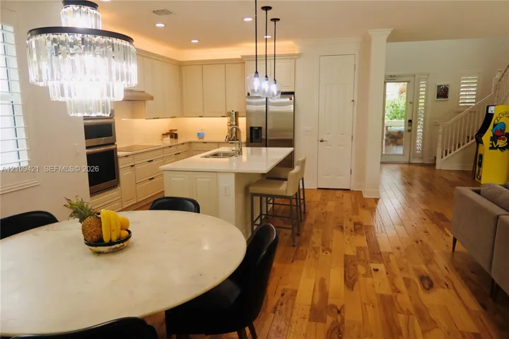 Kitchen featuring light-toned cabinetry, a center island with a stone countertop, wood-finish flooring, stainless steel built-in double wall ovens, and decorative glass pendant lighting