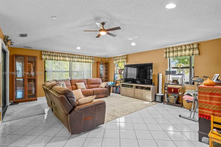 Living area featuring white ceramic tile flooring, a vaulted ceiling with a central fan, recessed lighting, and built-in wood cabinetry