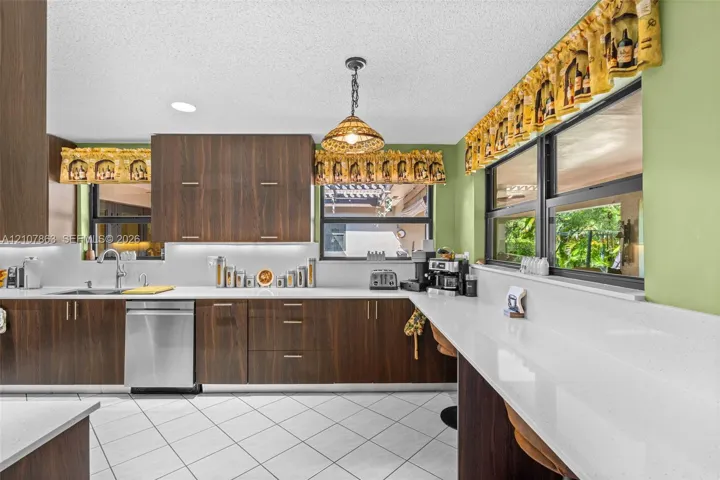 Kitchen featuring wood-finish cabinetry, white solid-surface countertops, stainless steel dishwasher, pendant lighting, and ceramic tile flooring