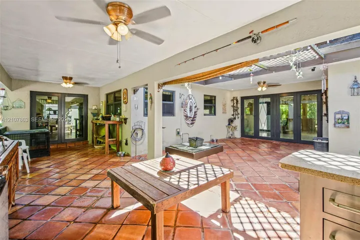 Covered outdoor patio featuring terra cotta tile flooring, multi-pane glass doors, built-in cabinetry, and dual ceiling fans