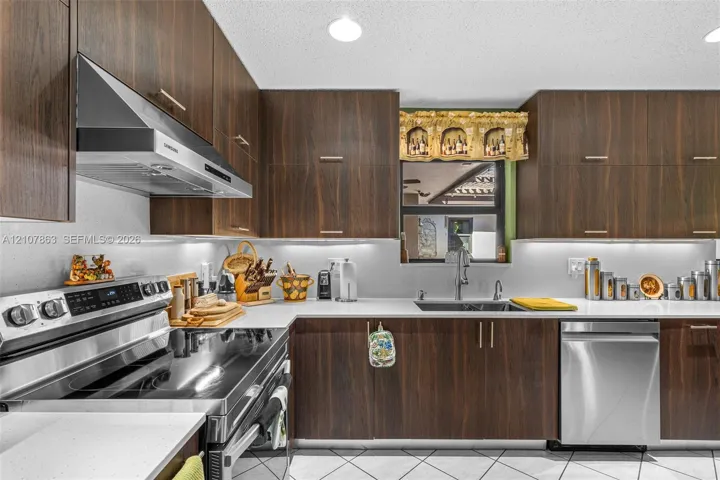 Kitchen featuring full-height dark wood-finish cabinetry, solid surface countertops, stainless steel appliances, a stainless steel undermount sink, and under-cabinet lighting