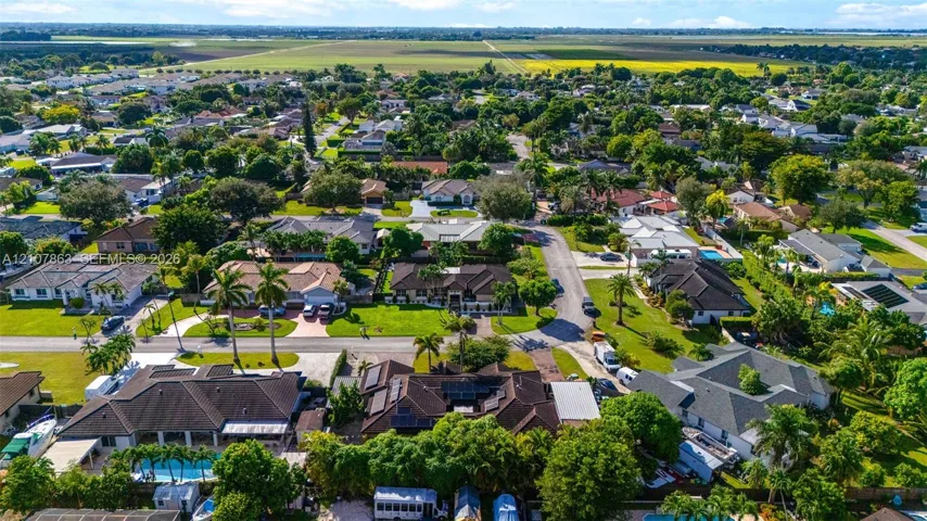 Aerial perspective of a residential neighborhood featuring mature canopy trees, manicured lawns, paved streets, and diverse single-story architectural styles