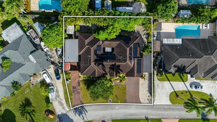 Aerial perspective of a property featuring a multi-gabled roof, paved driveways, established trees, and solar panel arrays