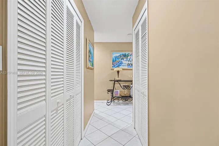 Hallway featuring white tiled flooring and dual white louvered closet doors